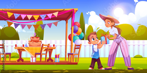 Birthday party on backyard with woman gives gift box boy. Vector cartoon illustration of garden with festive decoration, wooden tent, cake with candles, balloons and happy child