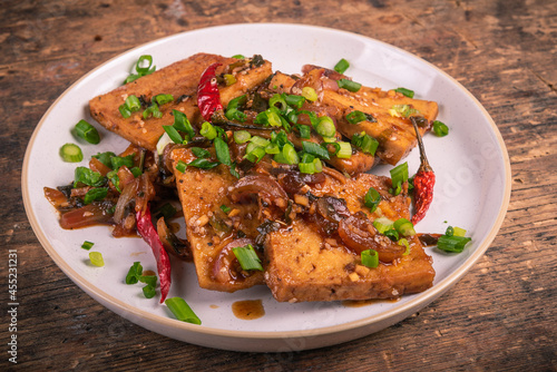 Spicy fried tofu with onion and hot chili sauce in a plate, close-up