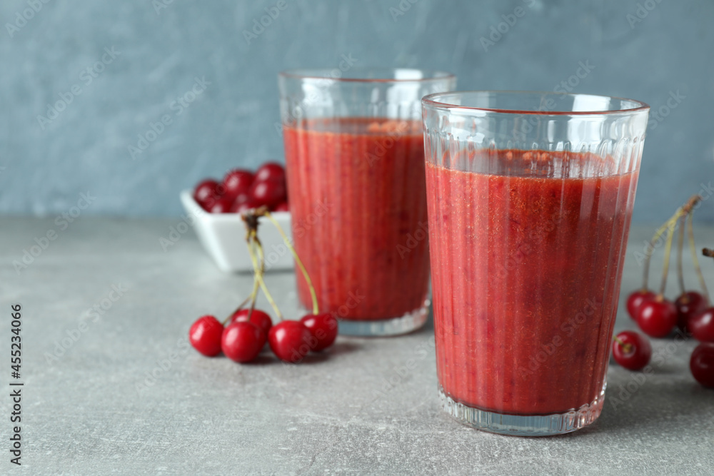 Glasses of cherry smoothie and ingredients on gray textured table Glasses of cherry smoothie and ingredients on gray textured table