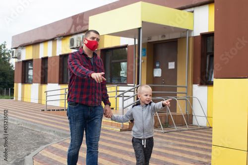 Dad takes his son to the doctor. Against the backdrop of a standard hospital building, father and son prepare for an examination. Concept of a single parent preparing a child for school or kindergarte