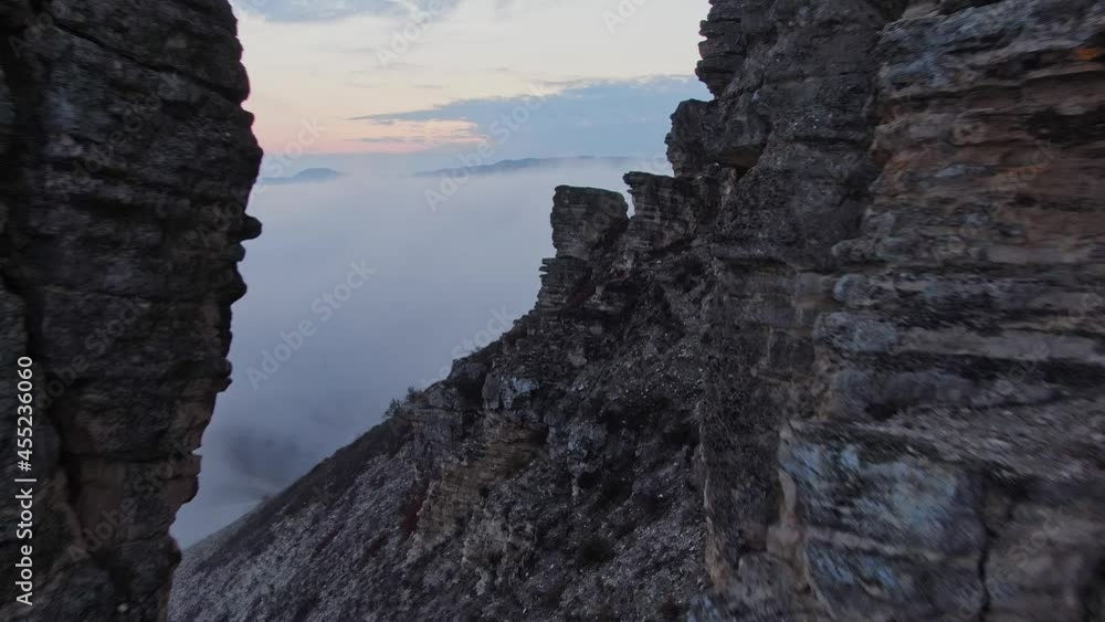 Aerial view. Drone Flying Along the Cliff with Traces of Weathered Soil on the Background of Fog and the Sky Lit by the Sunset. Aerial view. Drone Flying Along the Cliff with Traces of Weathered Soil on the Background of Fog and the Sky Lit by the Sunset.