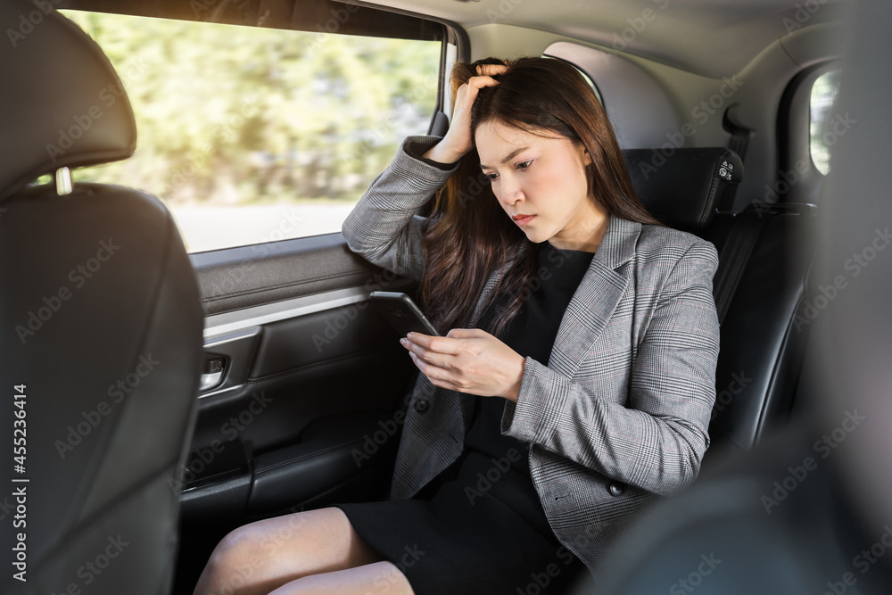 stressed business woman using a smartphone while sitting in the back seat of car