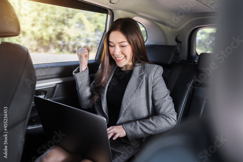 successful business woman using laptop computer while sitting in the back seat of car