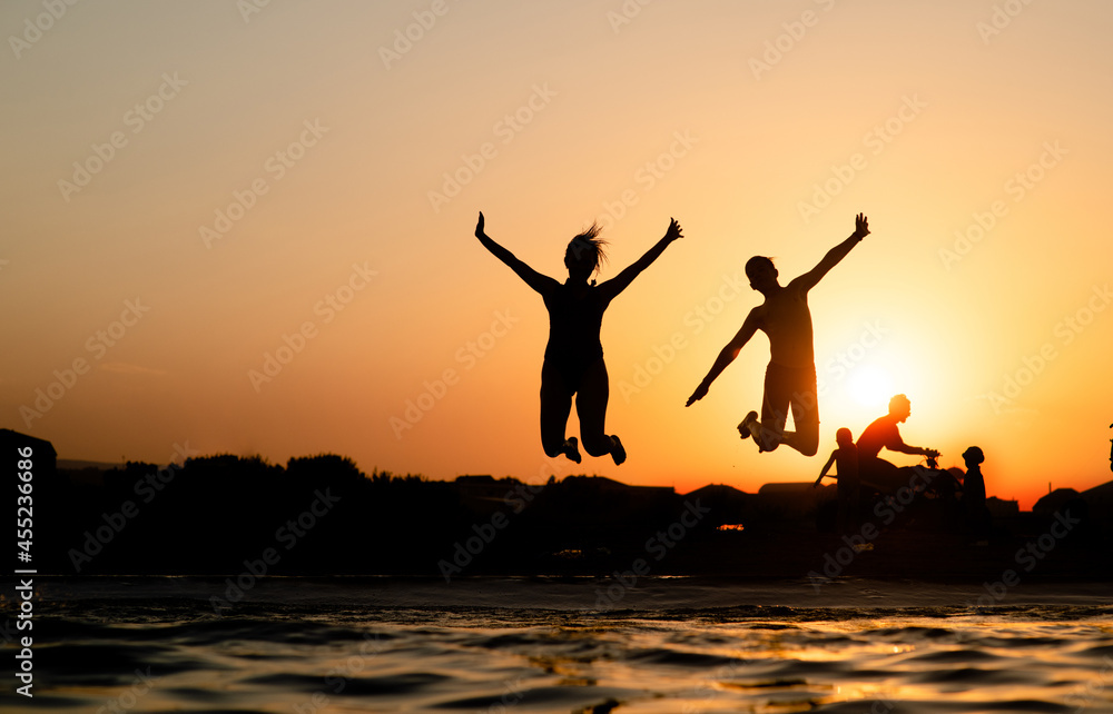 Fototapeta premium Joyful friends are having fun and jump at sunset beach in sunlight. Empty space for text