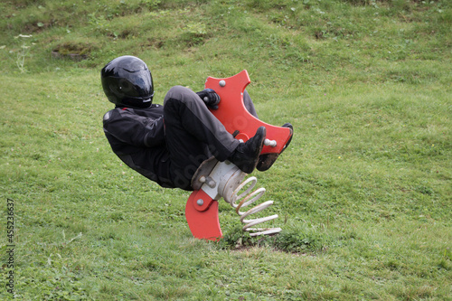 motorcyclist in black motorcycle clothing is sitting on a rocking horse on children's playground and is going crazy