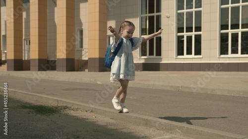 Happy little girl playing in the schoolyard, a little kid with a backpack, a child's school bag on the baby's shoulders, a fun child's primary education, a childhood dream, a fun school life © Валерий Зотьев