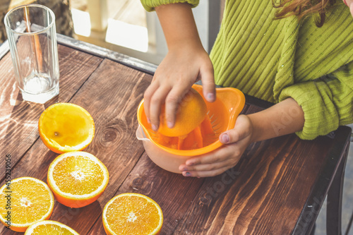 the girl child makes freshly squeezed orange juice on a manual juicer