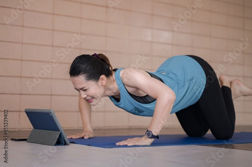 Asian woman in sports outfits worksout following online training program via digital tablet at home photo