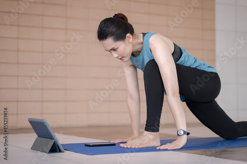 Asian woman in sports outfits worksout following online training program via digital tablet at home photo