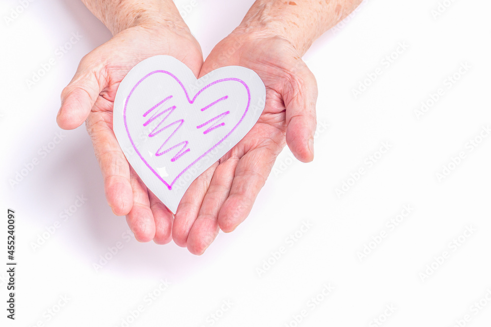 White paper cut a heart shape on the palm of a senior woman with a white background. Healthcare, World heart day, World health day. Valentine's day. People, age, love, and healthcare concept