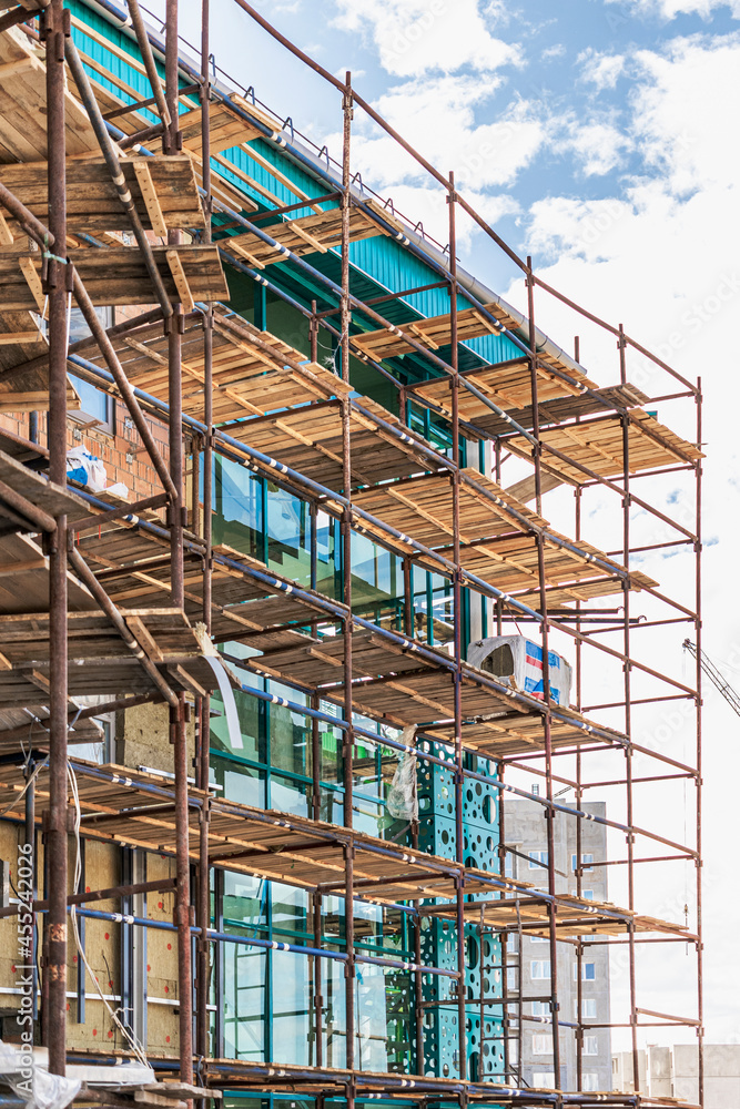 Fototapeta premium Scaffolding and scaffolding with wooden decks, against a blue sky. Performing construction work at height. Construction safety.