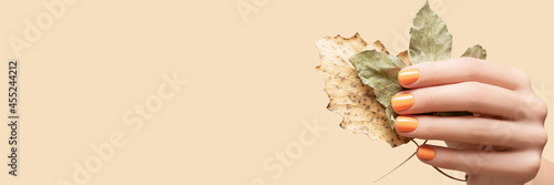 Female hand with glitter autumn orange nail design. Woman hand hold two autumn leaves. Advertising banner. Banner ad.
