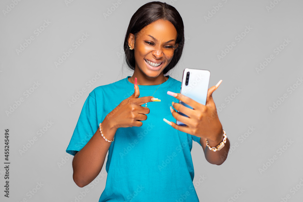 beautiful young african lady looking and pointing to her phone screen in excitement beautiful young african lady looking and pointing to her phone screen in excitement
