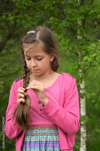 portrait of beautiful girl braiding braid against the background of green trees in  countryside. Close-up