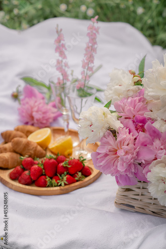 Outdoor picnic with champagne  strawberries  croissants and a bouquet of peonies