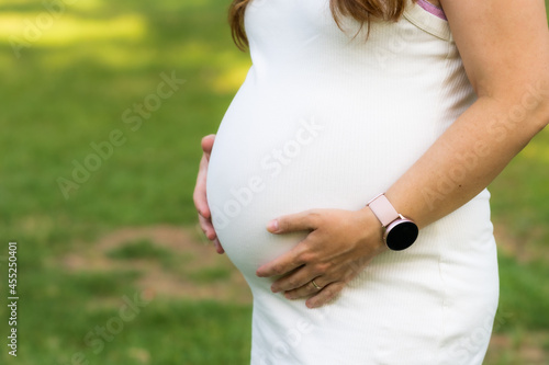 Close-up photo on the hands of a pregnant woman touching her belly outdoors