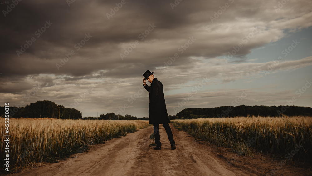 Young man in the field. He is wearing a black coat, hat and glasses. It's cloudy outside Young man in the field. He is wearing a black coat, hat and glasses. It's cloudy outside