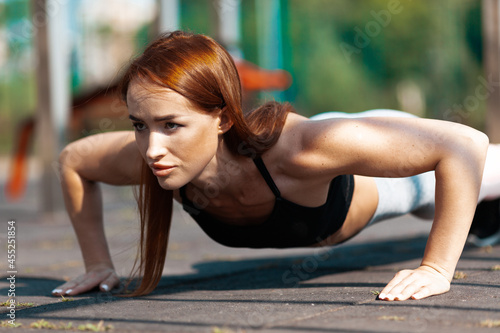 The red-haired girl does push-ups. Sports activities in a special place. The trainer.shows exercises to support good health.