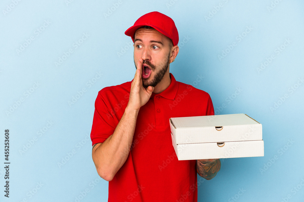 Young caucasian delivery man with tattoos holding pizzas isolated on blue background is saying a secret hot braking news and looking aside Young caucasian delivery man with tattoos holding pizzas isolated on blue background is saying a secret hot braking news and looking aside