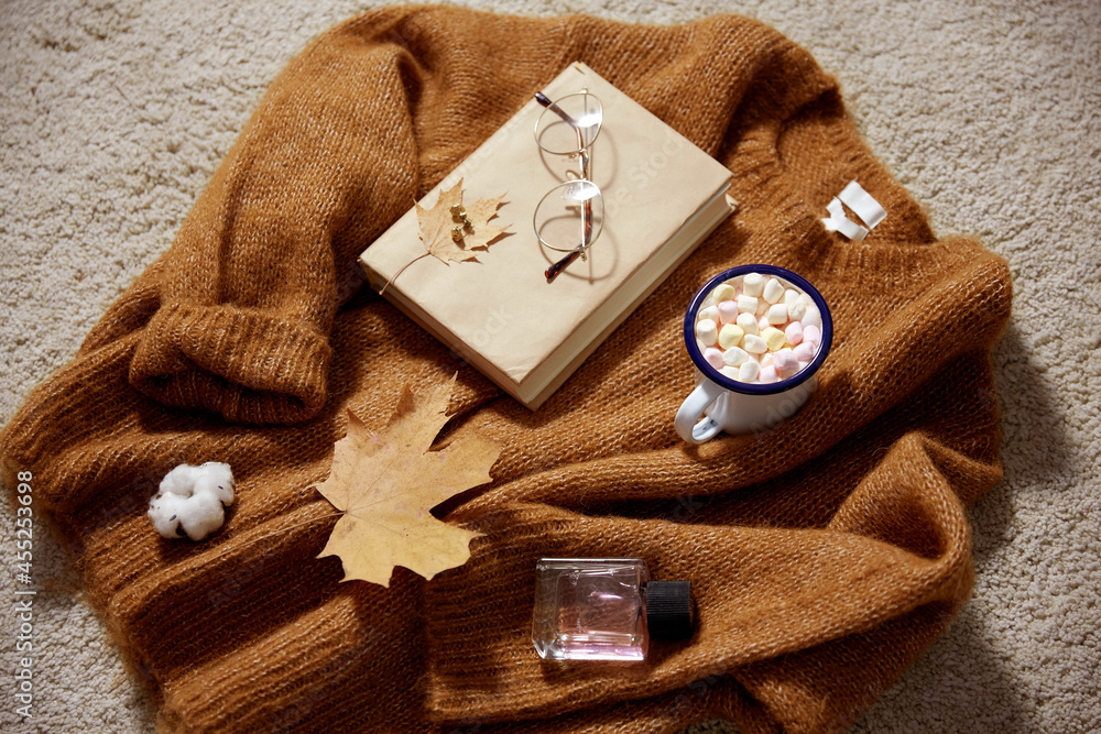 season, leisure and objects concept - camp mug full of marshmallow, book, glasses and autumn leaves on sweater season, leisure and objects concept - camp mug full of marshmallow, book, glasses and autumn leaves on sweater