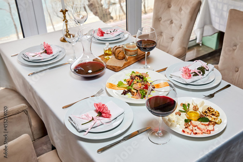 A decorated restaurant table with glasses of red wine and appetizer awaits guests. Close-up