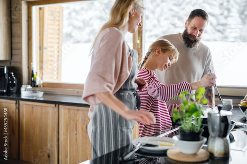 Family with small daughter cooking indoors, winter holiday in private apartment.
