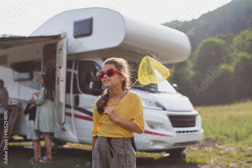 Happy small girl with sunglasses standing outdoors by caravan car, family holiday trip.