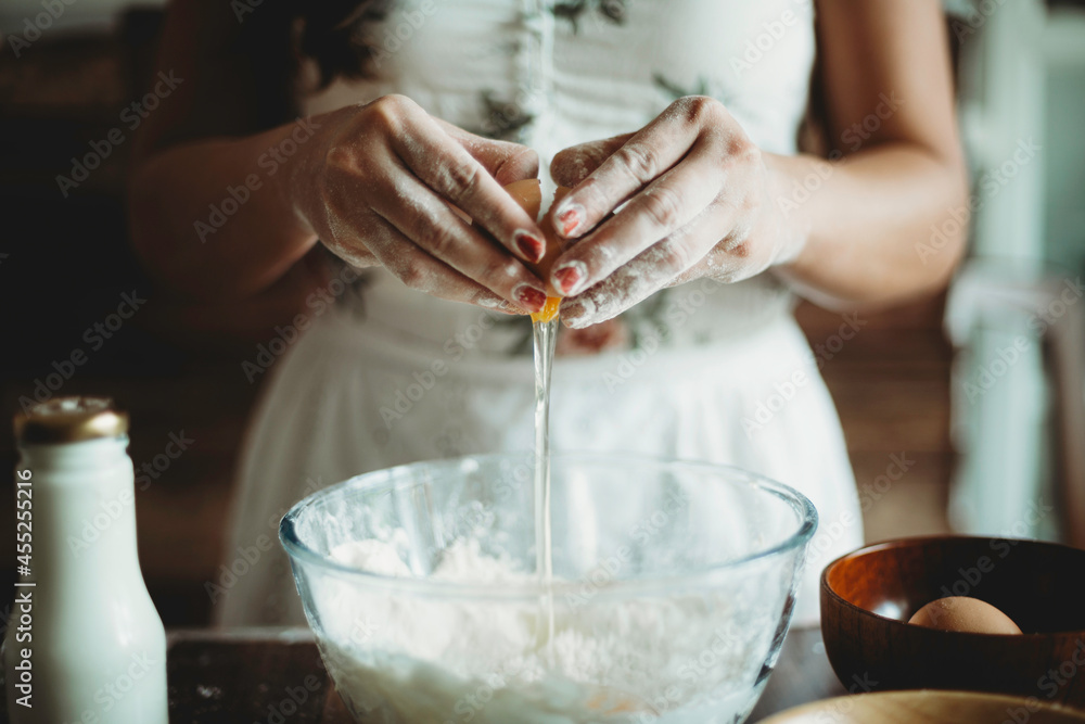 Woman cracking egg for baking.Bake preparation production.Person's hands crack organic egg.Pastry and culinary.Healthy home dessert by baker.Recipe for cake or cupcake dough in glass bowl.