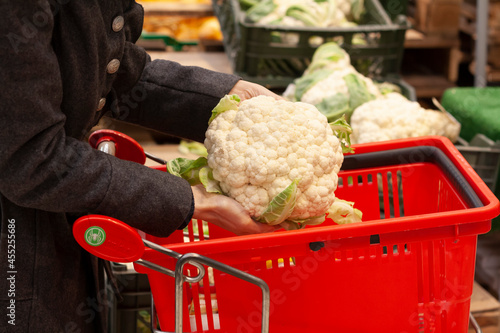 A woman buys cauliflower in a supermarket and puts it in a basket