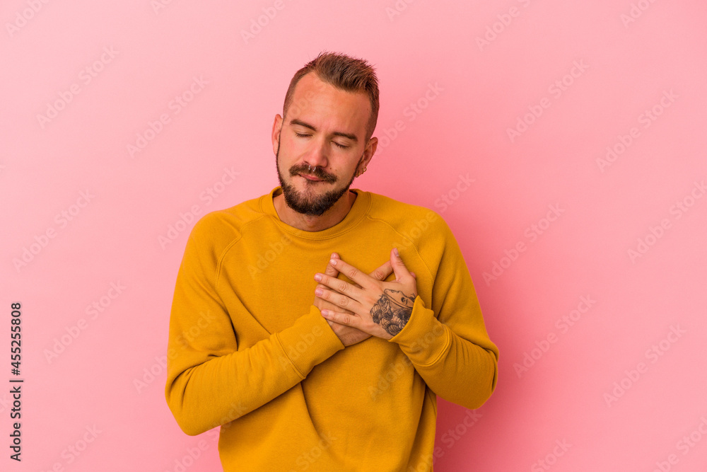 Fototapeta premium Young caucasian man with tattoos isolated on pink background has friendly expression, pressing palm to chest. Love concept.