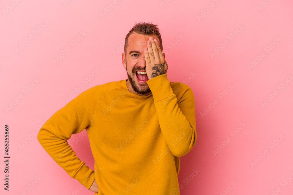 Young caucasian man with tattoos isolated on pink background having fun covering half of face with palm. Young caucasian man with tattoos isolated on pink background having fun covering half of face with palm.
