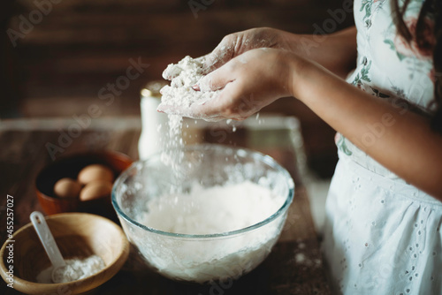 Lady's hands sprinkling and pouring flour into mixing glass bowl.Worker preparing dough.Professional baker in bakehouse.Kneading process.Woman preparing cake baking ingredients.