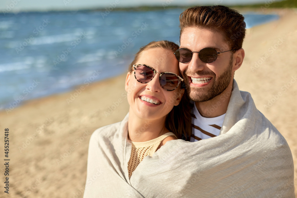 leisure, relationships and people concept - happy couple in sunglasses covered with blanket hugging on summer beach