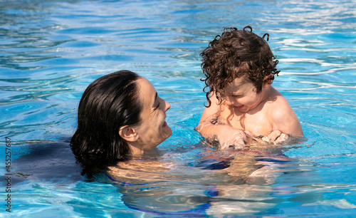 4-5 year old boy with his mom in the pool smiling and enjoying himself