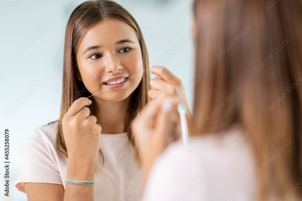 dental care, hygiene and people concept - happy smiling teenage girl with floss cleaning teeth and looking in mirror at bathroom dental care, hygiene and people concept - happy smiling teenage girl with floss cleaning teeth and looking in mirror at bathroom