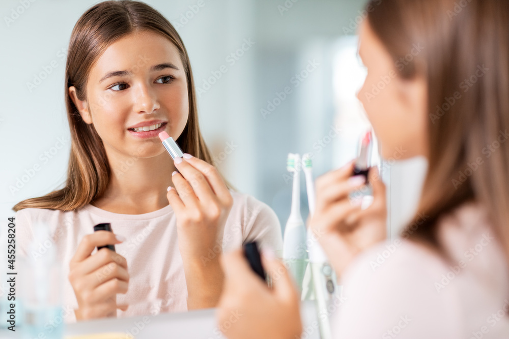 beauty, make up and cosmetics concept - teenage girl applying lipstick and looking to mirror at home bathroom beauty, make up and cosmetics concept - teenage girl applying lipstick and looking to mirror at home bathroom