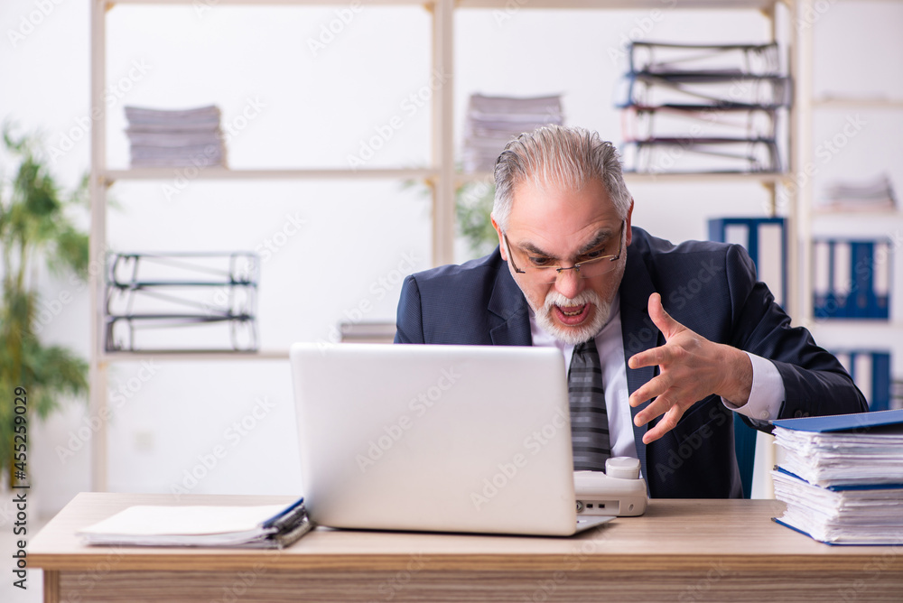Old male employee unhappy with excessive work in the office Old male employee unhappy with excessive work in the office