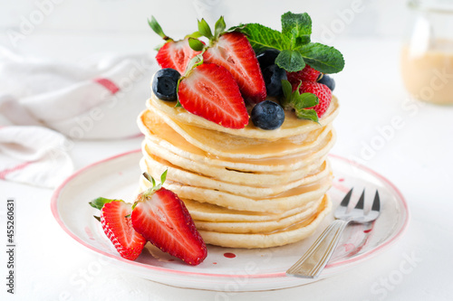 Breakfast pancakes. Stack of pancakes with fresh blueberries and strawberries on plate with bowls of strawberries and blueberries on light slate, stone or concrete background. Top view. copy space