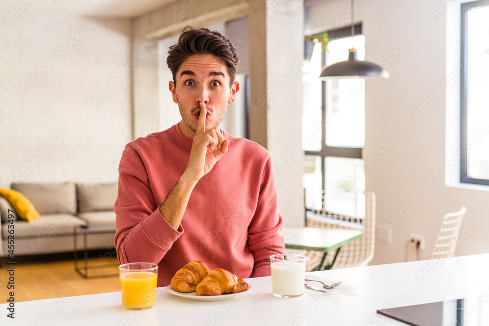 Young mixed race man having breakfast in a kitchen on the morning keeping a secret or asking for silence. Young mixed race man having breakfast in a kitchen on the morning keeping a secret or asking for silence.