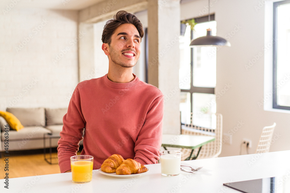 Young mixed race man having breakfast in a kitchen on the morning looks aside smiling, cheerful and pleasant. Young mixed race man having breakfast in a kitchen on the morning looks aside smiling, cheerful and pleasant.