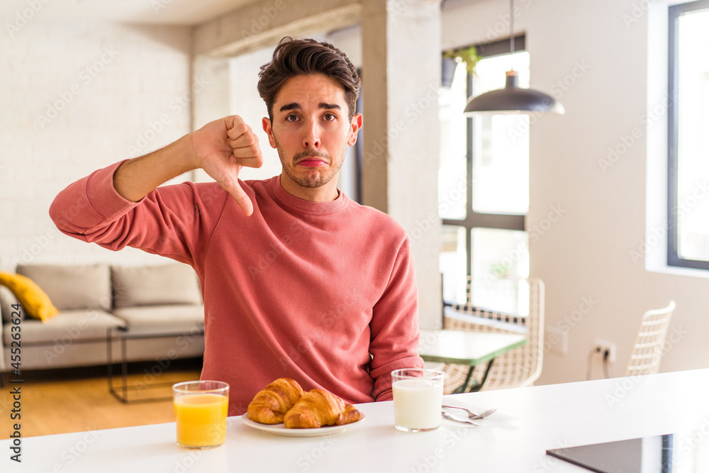 Young mixed race man having breakfast in a kitchen on the morning showing a dislike gesture, thumbs down. Disagreement concept. Young mixed race man having breakfast in a kitchen on the morning showing a dislike gesture, thumbs down. Disagreement concept.