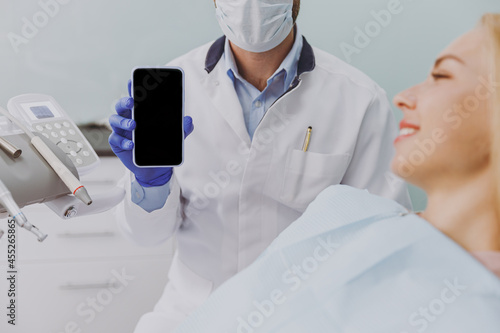 Принти на полотні Young friendly man dentist show mobile cell phone with blank screen area near pa