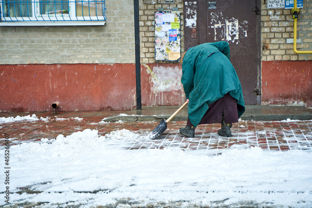 An old grandma yard man clears the snow on entrance