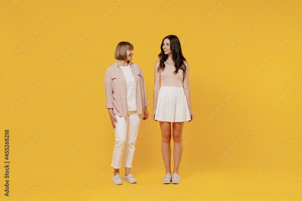 Full body two young smiling fun daughter mother together couple women in casual beige clothes looking to each other isolated on plain yellow color background studio portrait Family lifestyle concept. Full body two young smiling fun daughter mother together couple women in casual beige clothes looking to each other isolated on plain yellow color background studio portrait Family lifestyle concept.