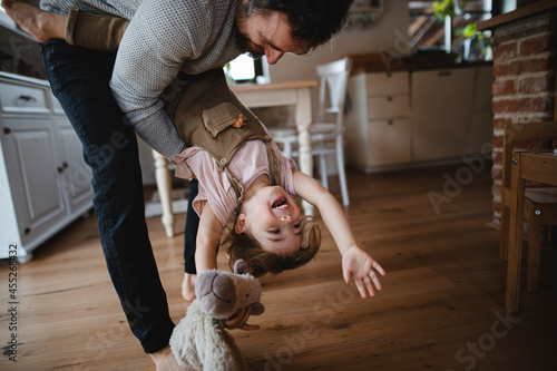 Mature father with small daughter playing indoors at home, holding her upside down.