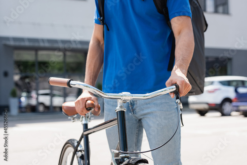 Cropped view of courier with thermo backpack standing near bicycle outdoors
