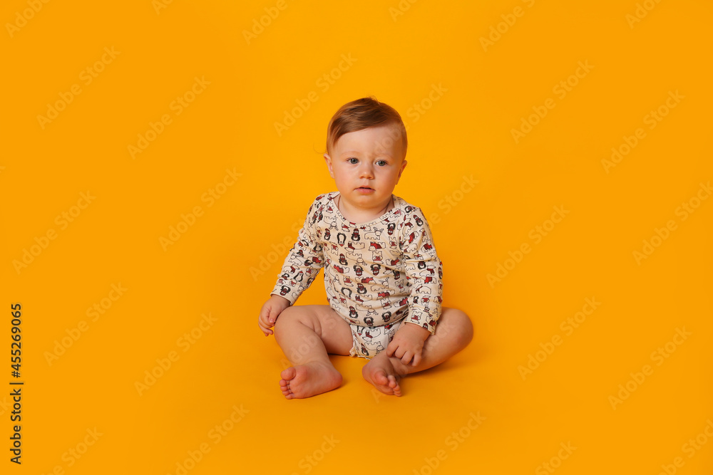 a beautiful little blue-eyed boy with light red hair in a bodysuit sits on a yellow background a beautiful little blue-eyed boy with light red hair in a bodysuit sits on a yellow background