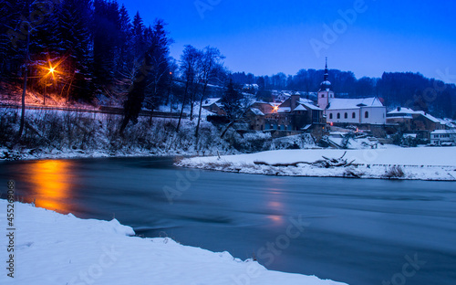 paysage hivernal de Chassepierre peu après le coucher du soleil (heure bleue) présentant une rivière en avant plan de la ville enneigée photo