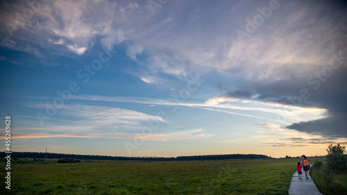 Photographie de paysage d'une maman et son enfant en randonnée dans les hautes fagnes (Belgique) sous un ciel chargé de fin de journée (coucher du soleil)