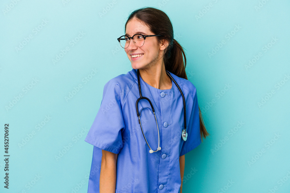 Young caucasian nurse isolated on blue background looks aside smiling, cheerful and pleasant. Young caucasian nurse isolated on blue background looks aside smiling, cheerful and pleasant.